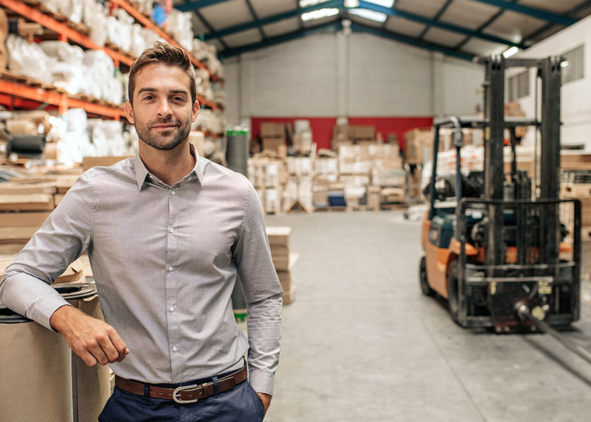 A small business owner stands in a warehouse, with textiles and a forklift in the background.